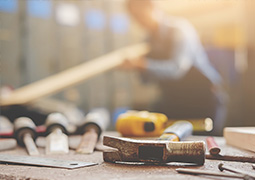 Werkzeuge liegen auf dem Tisch, in Hintergrund arbeitet jemand mit Holz.