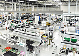 Eine große Halle mit verschiedenen Arbeitsplätzen, die Menschen tragen weiße Kittel.